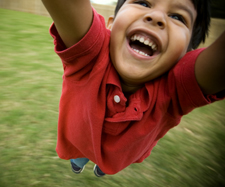 little boy smiling while spinning around on the playground outside